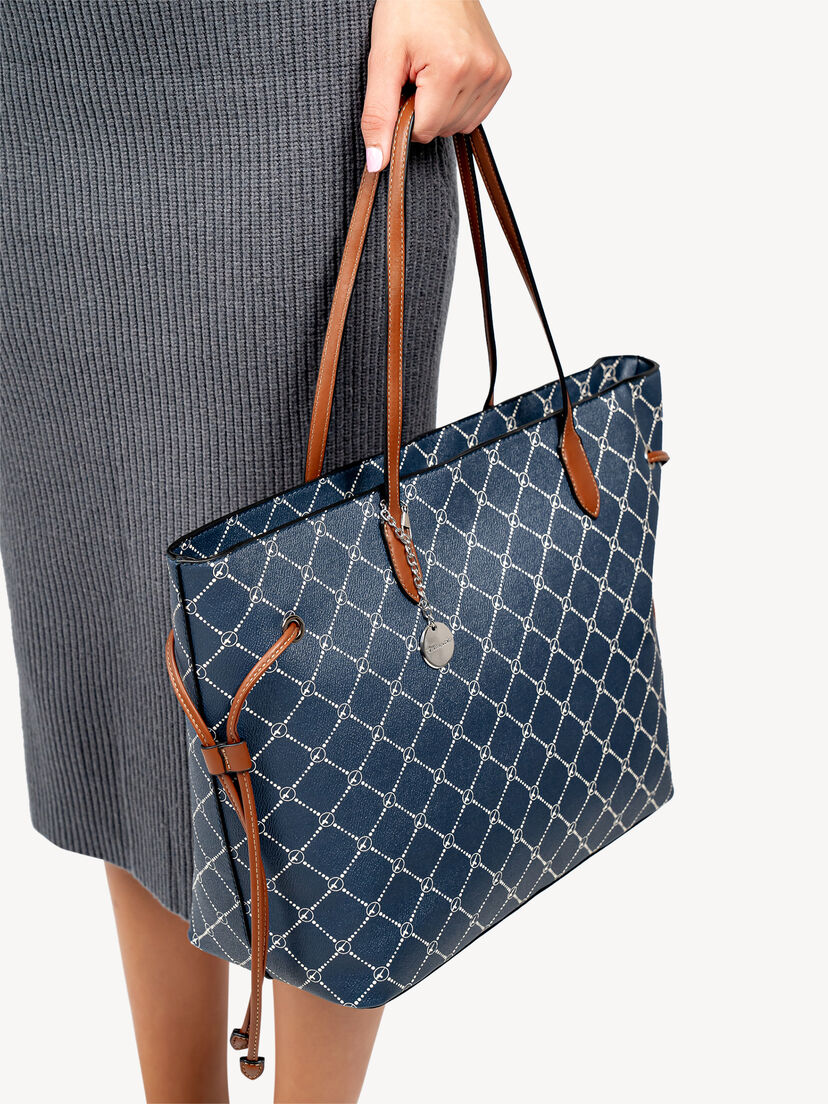 Detail van blauwe shopper tas met bruine leren handvatten en zilveren bedel aan hand van vrouw